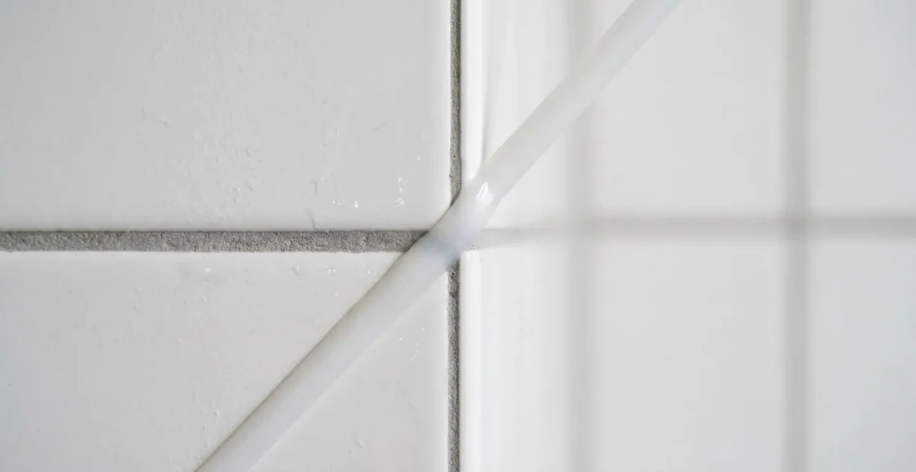 Close-up photograph of bathroom tile grout and silicone sealant junction showing maintenance condition