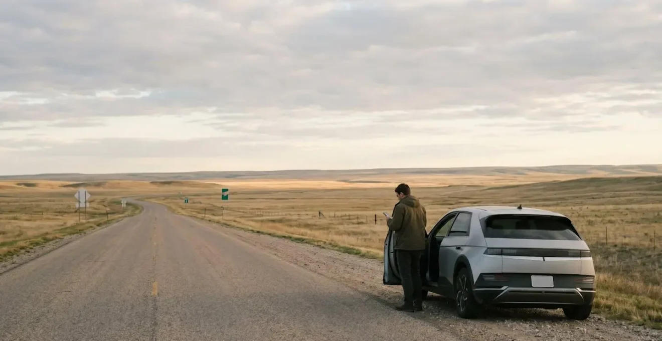 Wide environmental scene showing electric vehicle in remote location emphasizing range and charging infrastructure challenges