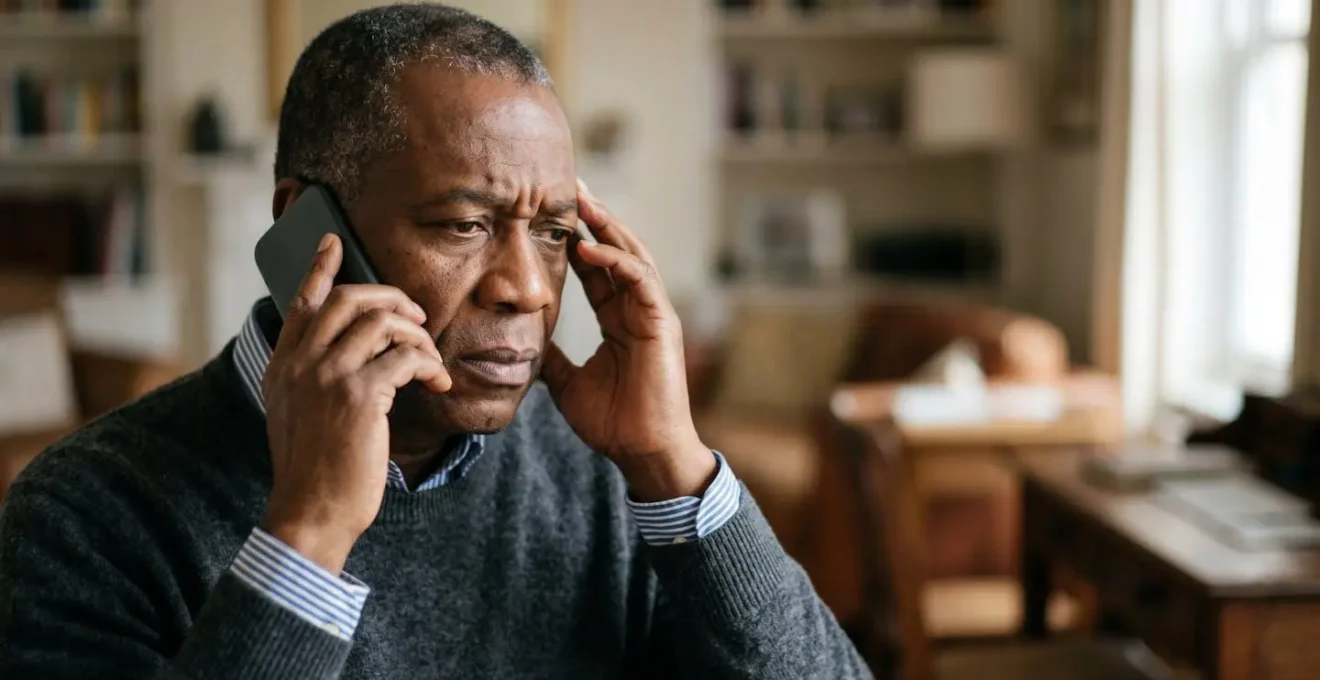 Person holding smartphone to ear with concerned expression, soft window lighting emphasizing emotional vulnerability during a potential fraud phone call