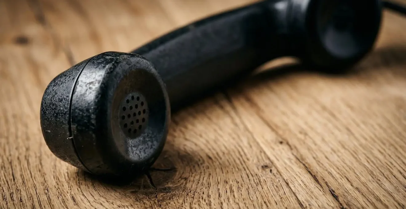 A vintage rotary telephone handset resting on a wooden surface with dramatic lighting creating strong shadows suggesting the danger of unsolicited cold calls